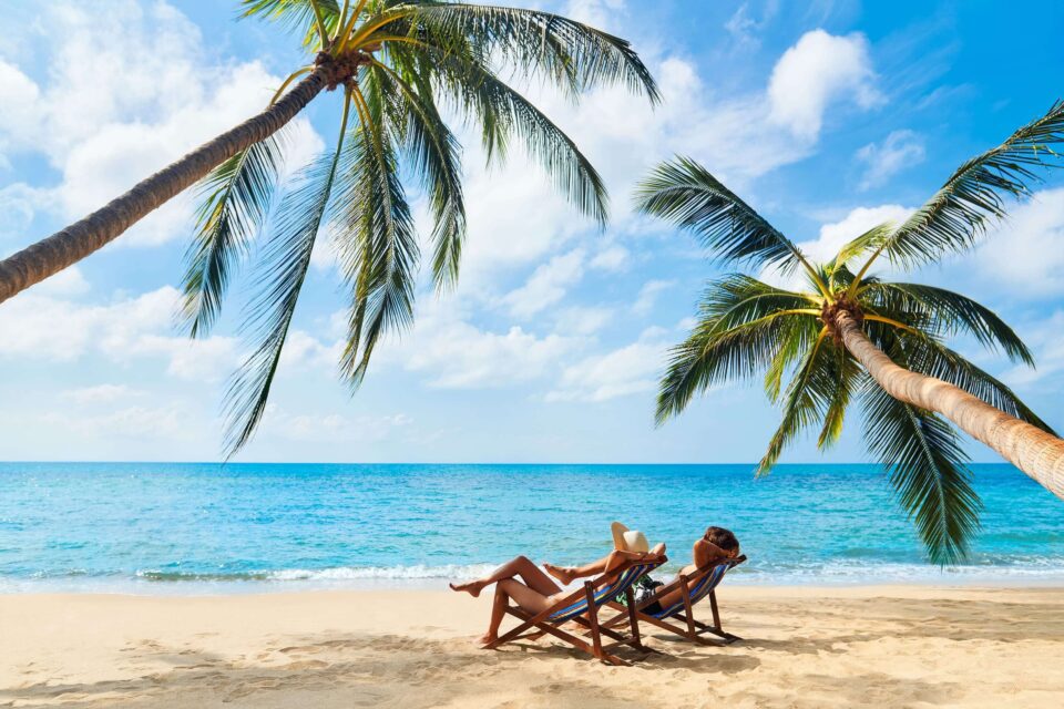 Couple Relaxing on Beach Loungers Under Palm Trees